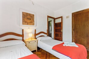 A room with two single beds, a nightstand with a lamp, a wooden door, and a wall-mounted artwork. - Self catering La Casona de la Garaba for 14 people (Grado)