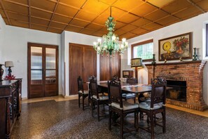 A dining area with a wooden table and chairs, a chandelier, a fireplace, and a painting on the wall.