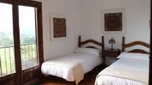 Habitación con dos camas, cabecera de madera, mesita de noche con lámpara y ventana con vista a zonas verdes.