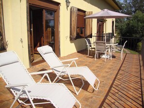 Une terrasse avec des chaises longues blanches, une table et un parasol.