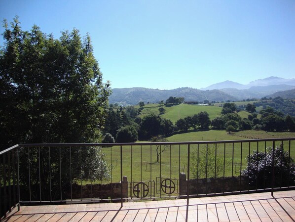A balcony with a view of a green landscape, including hills and trees.