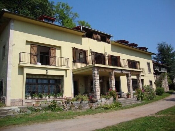 Un edificio a due piani con balconi, una base in pietra e un vialetto lastricato.