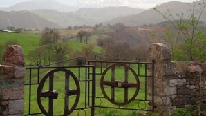 Una puerta rústica con diseño de metal, frente a un paisaje montañoso y un campo en primer plano.