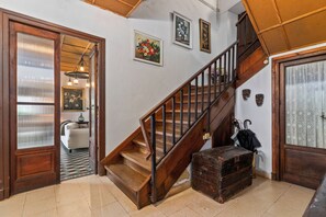 Escadaria com corrimãos de madeira, um sofá branco, um tapete estampado e um baú antigo.