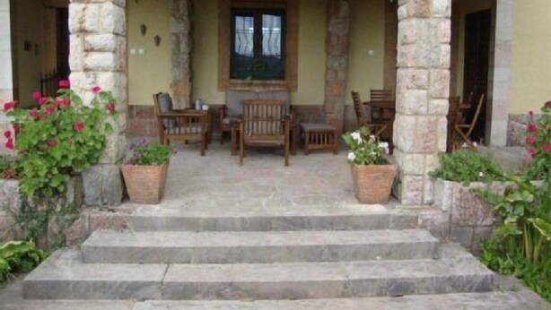 Una escalera de piedra que lleva a un porche con mobiliario de madera y plantas en macetas.