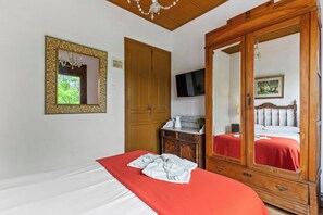A bedroom with a bed, a wardrobe, a television, and a mirror.