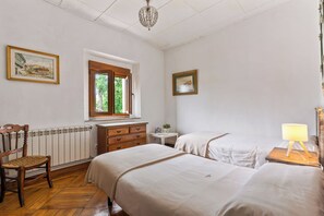 Une chambre avec deux lits, une commode en bois, une chaise, une fenêtre donnant sur un beau paysage et un lustre.