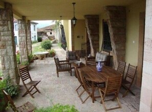 Una veranda riparata con tavolo e sedie in legno, pilastri in pietra e vista sui dintorni.
