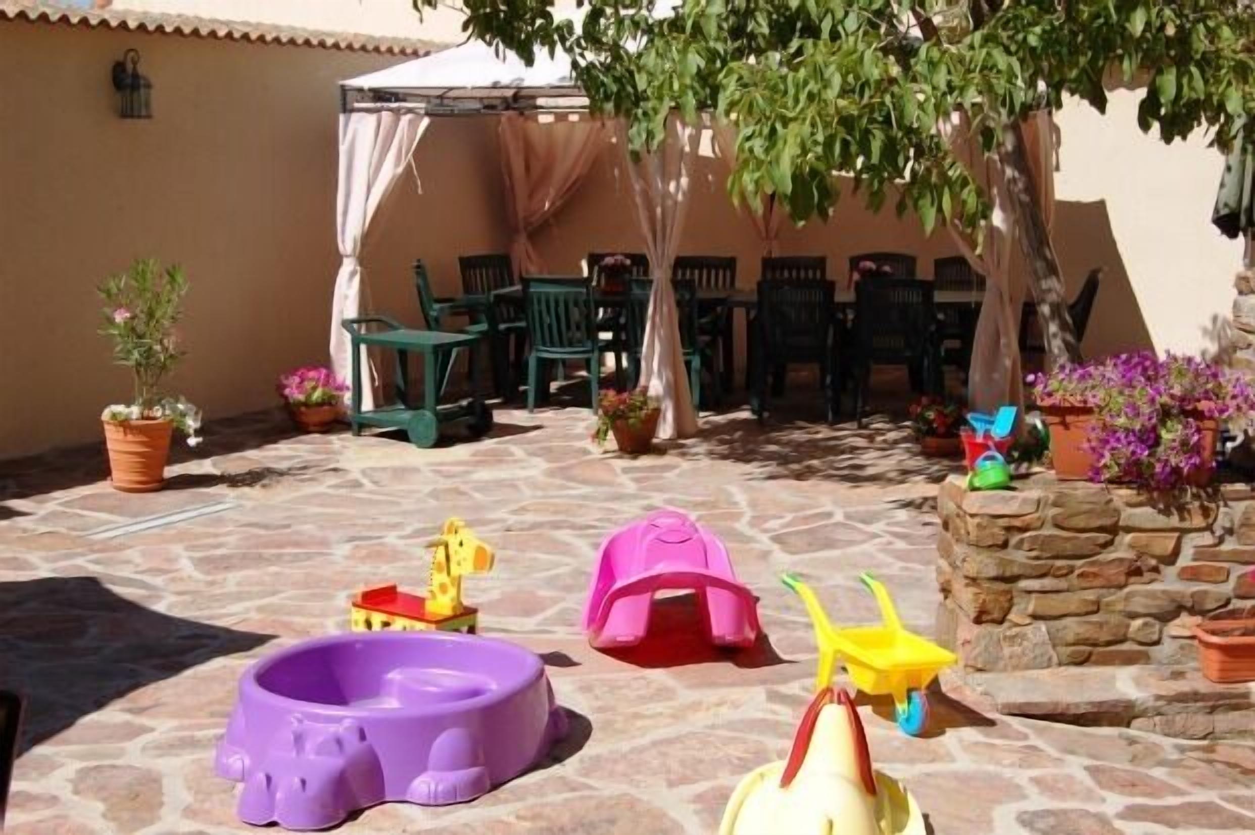 A patio area with stone flooring, green plastic chairs, a white canopy, and potted plants.