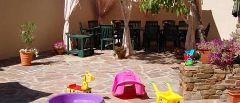 A patio area with stone flooring, green plastic chairs, a white canopy, and potted plants.