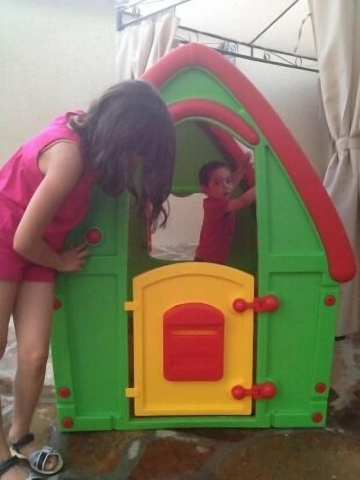Un enfant joue à l’intérieur d’une maison de jeu colorée, dont la porte est verte et jaune.