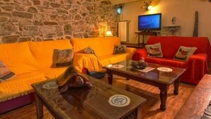 A cozy living room with a stone wall, two sofas, a coffee table, and a television. - Cottage Sunsets for 16 people (full rental) (Migueláñez)