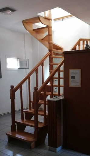 Un escalier en colimaçon en bois, doté d’un palier, d’une plaque fixée au mur et d’une fenêtre avec des stores.