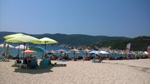 A beach with umbrellas and chairs, a clear sky, and a mountainous backdrop. - Beautiful holiday house 400 m to the beach! (Nea Kallikratia)
