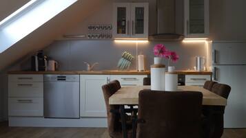 Eine moderne Küche mit Dachfenster, weißen Schränken, einem Holztisch und braunen Stühlen.