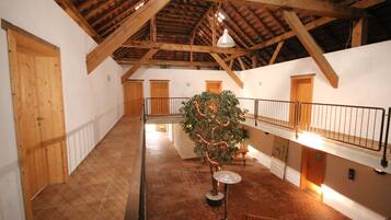Ein geräumiger Innenraum mit hohen Decken und Holzbalken, mit einem zentral platzierten Baum mit Lichtern, einer Treppe und einem Geländer, das den Bereich überblickt.