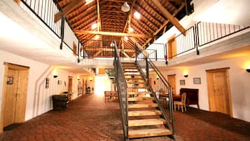 Ein geräumiger Saal mit Terrazzoboden, Holzwänden und einer zentralen Treppe mit Metallgeländern.