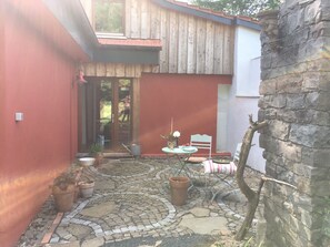 Een patio met een vloer van stenen mozaïek, een tafel met stoelen, potplanten en een stenen muur.