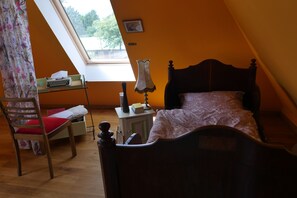 Een slaapkamer met een houten bed, een bureau met een schrijfmachine, een lamp en een raam met uitzicht op bomen.