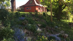 Een rode woning, omringd door weelderige begroeiing en bloeiende planten.