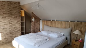A modern bedroom with a large bed, a wooden headboard, a bedside table with a lamp, and a wall-mounted shelf. - Family home 100m from the beach (Saint-Nazaire)