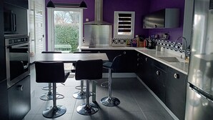 A modern kitchen with a dining area, featuring a large island, bar stools, and stainless steel appliances. - Family home 100m from the beach (Saint-Nazaire)