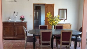 A dining area with a round table, six chairs, a vase with yellow flowers, a wooden cabinet, and a mirror on the wall.