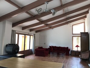 Uma sala de estar espaçosa com teto alto, vigas de madeira aparentes, um conjunto de sofá vermelho, uma mesa de centro de vidro e uma grande janela que proporciona iluminação natural.