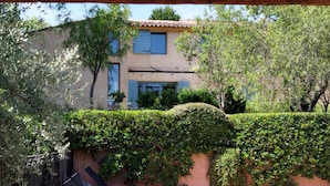 A building with a tiled roof, a balcony, and a hedge in front.