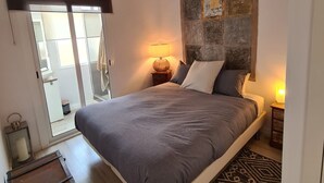 Ein Schlafzimmer mit einem Bett, einem Deckenventilator, einem Nachttisch mit Lampe, einem gemusterten Teppich und einer hölzernen Kommode.