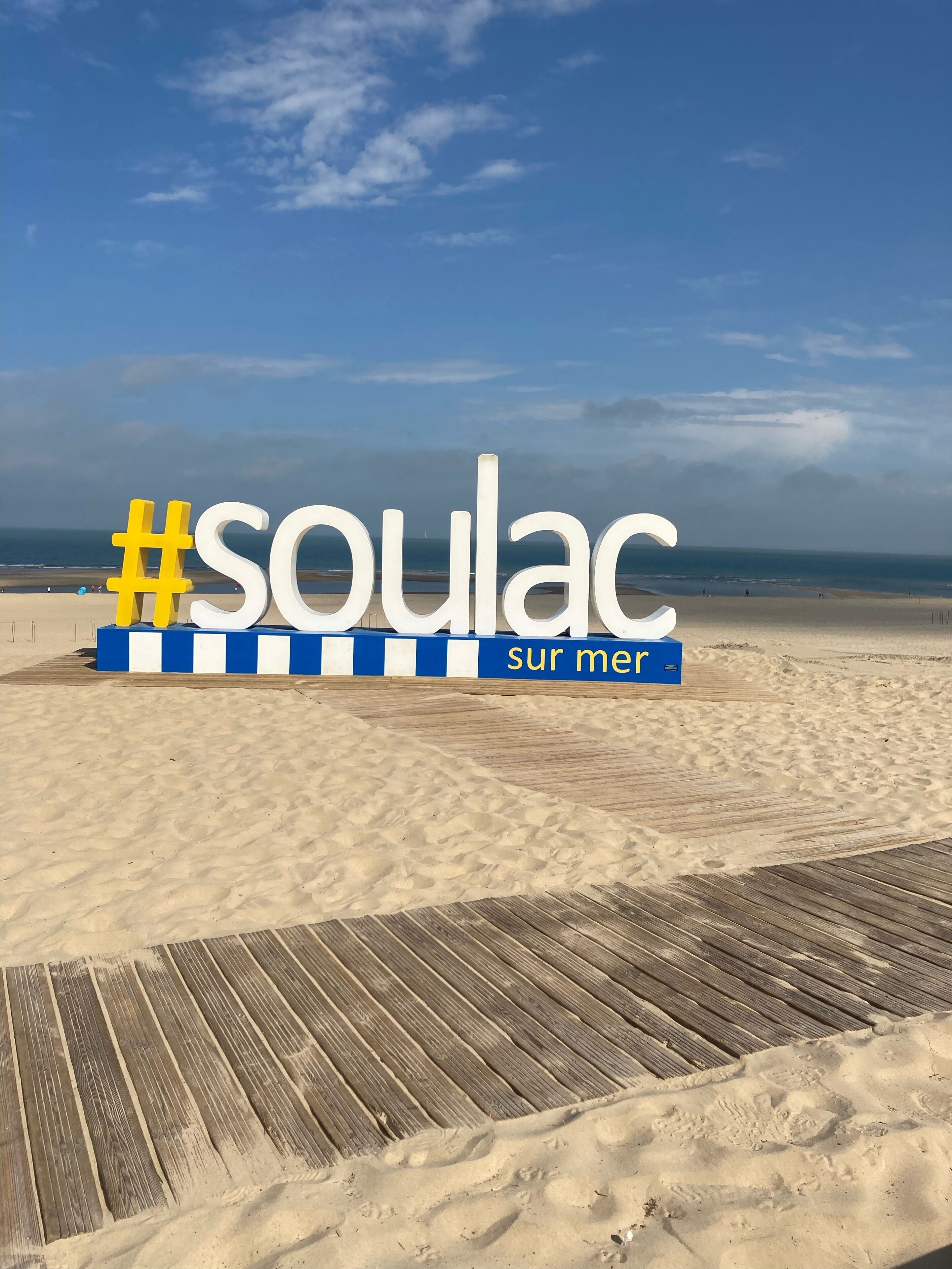 Une plage avec une promenade en bois et un panneau indiquant « Soulac-sur-Mer ».