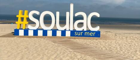 Une plage avec une promenade en bois et un panneau indiquant « Soulac-sur-Mer ».