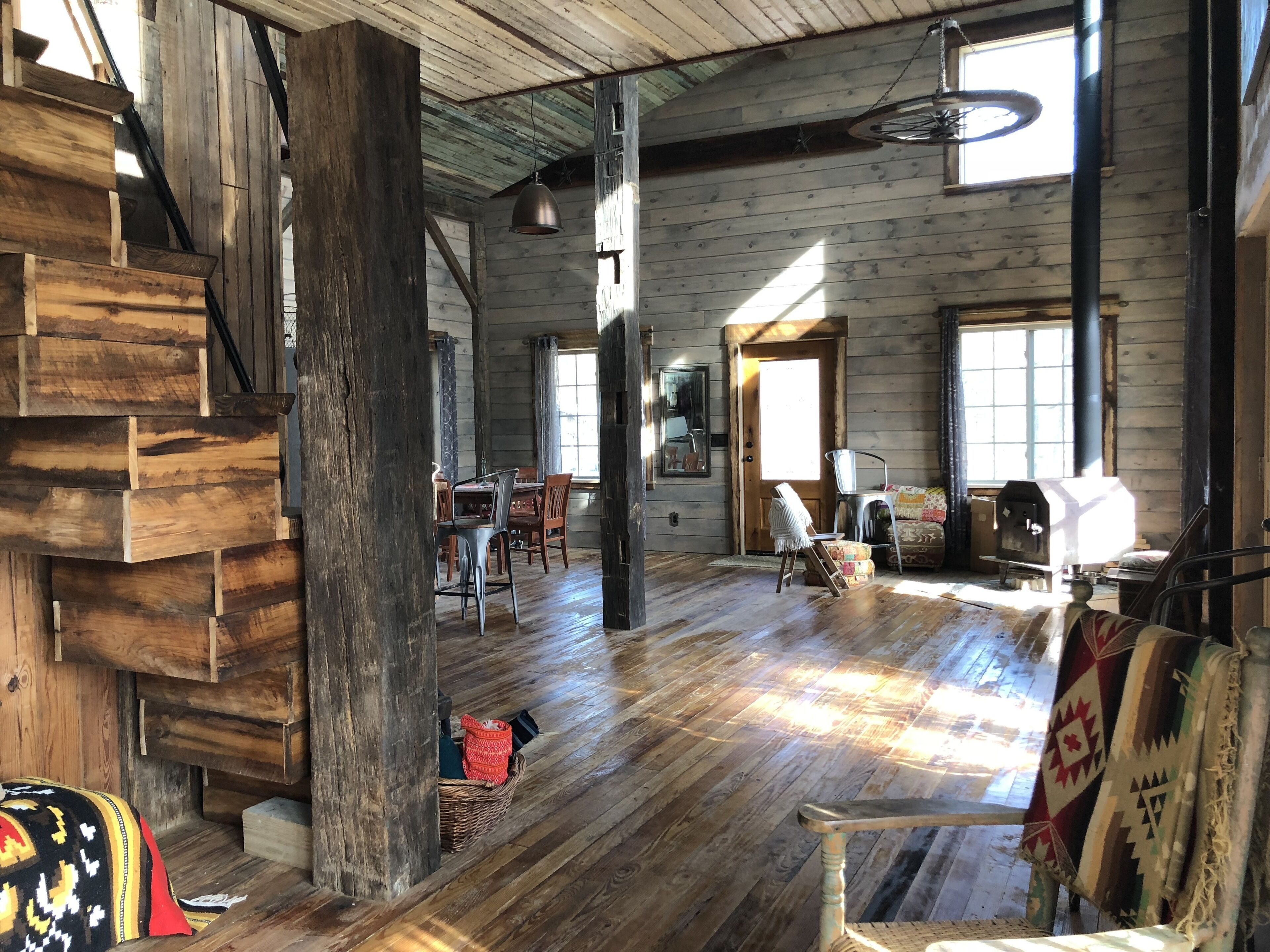 A rustic cabin interior with a wooden staircase, a dining area, and a large window allowing natural light.