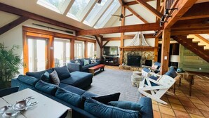 A spacious living area with a high ceiling, wooden beams, a fireplace, and a large window allowing natural light. - Bayfront Lodge-Beautiful & Unique East Bay Retreat (Gulf Breeze)