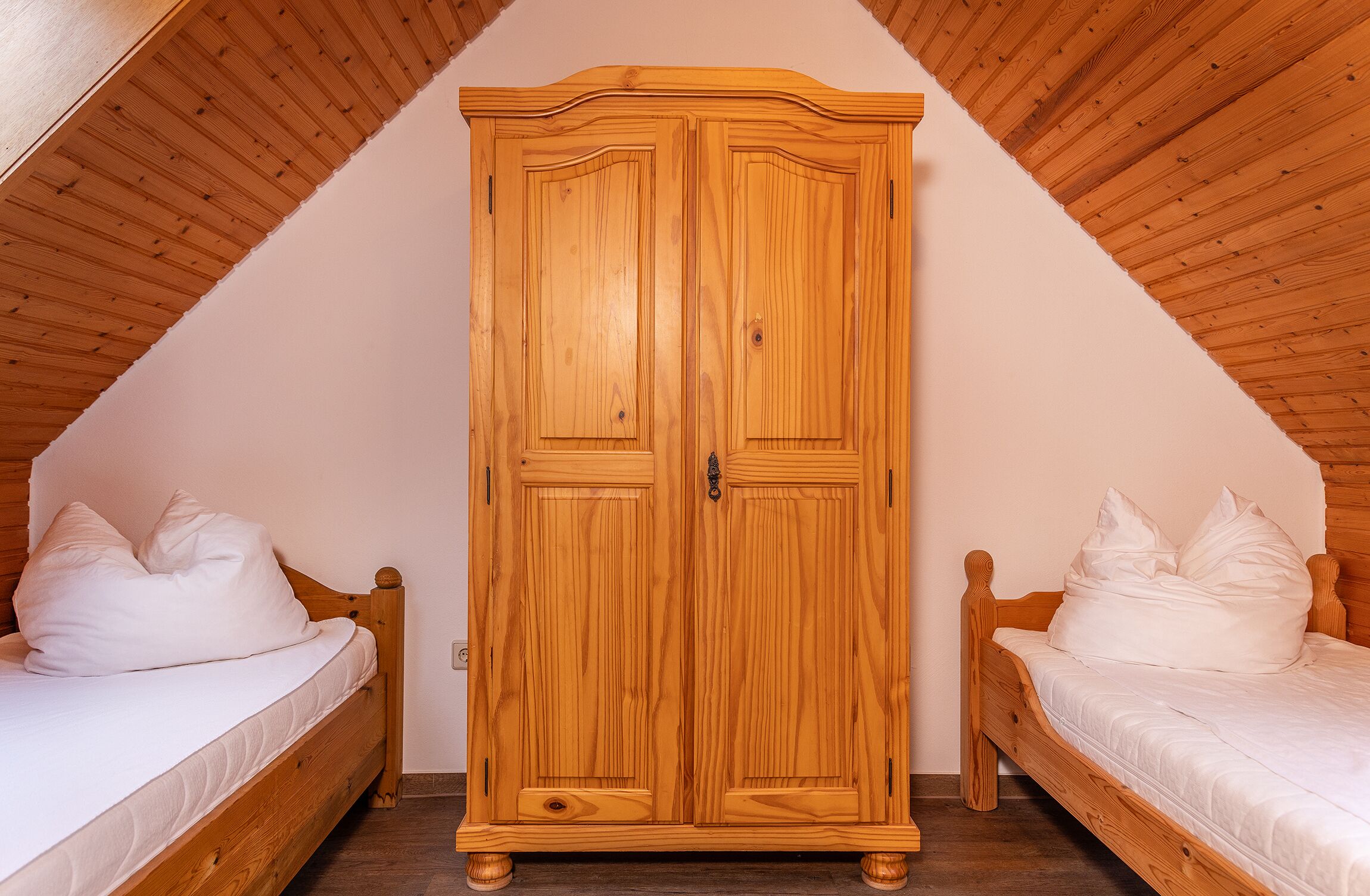 A bedroom with a wooden wardrobe, two single beds, and a sloped ceiling.