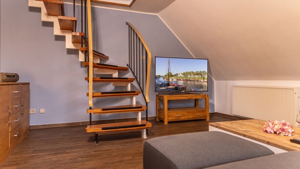 Ein modernes Wohnzimmer mit einer Holztreppe, einem Flachbildfernseher auf einem Holzboden und einer gemütlichen Sitzecke.