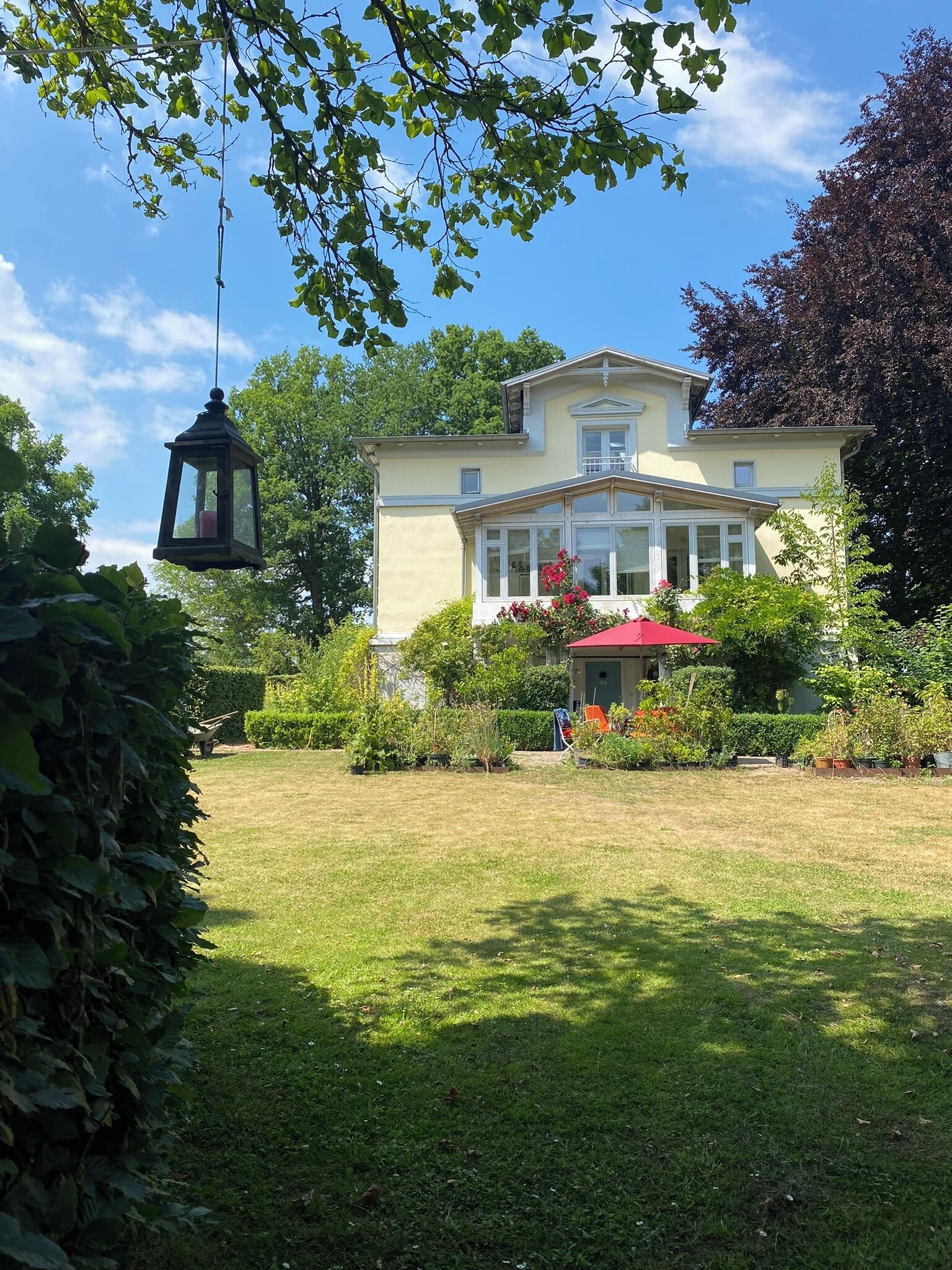 A two-story house with a garden in front, a hanging lantern, and a red umbrella.