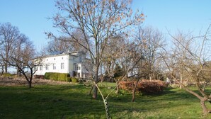 A white building with a symmetrical facade, surrounded by a well-maintained lawn and leafless trees. - quiet holiday overlooking the pond, park and forest edge (Niederklütz)