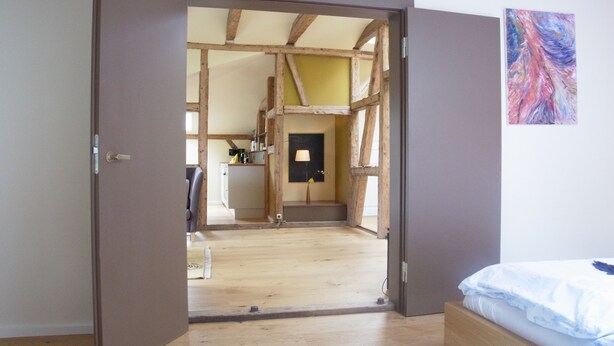 An open doorway leading to a room with a wooden ceiling and a bed with a white and blue patterned bedspread. - quiet holiday overlooking the pond, park and forest edge (Niederklütz)
