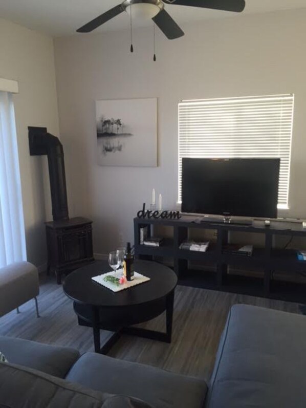 A modern living room with a large flat-screen TV, a ceiling fan, a fireplace, and a cozy seating area. - Oak Lane Cottage, Country Setting on Wine Route, Easy Access to NOTL (St. Catharines)