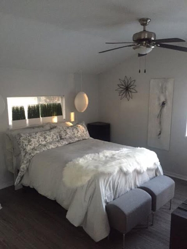 Un dormitorio con cama, ventilador de techo, ventana con vistas y una obra de arte en la pared.