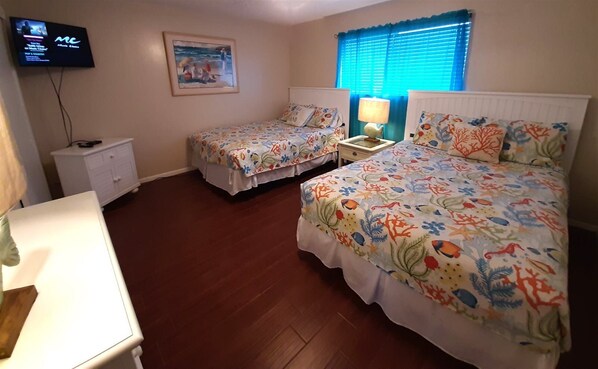 Habitación de hotel con dos camas, televisor, un cuadro y ventana con persianas.