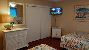 Une chambre à coucher avec un lit, une commode, un téléviseur et un tableau accroché au mur.