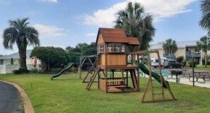 A playground with a wooden playhouse, slides, and swings. - Oasis #504 Free Beach Service Included - 2 Chairs and Umbrella 2-Bd 2-Bath (Destin)