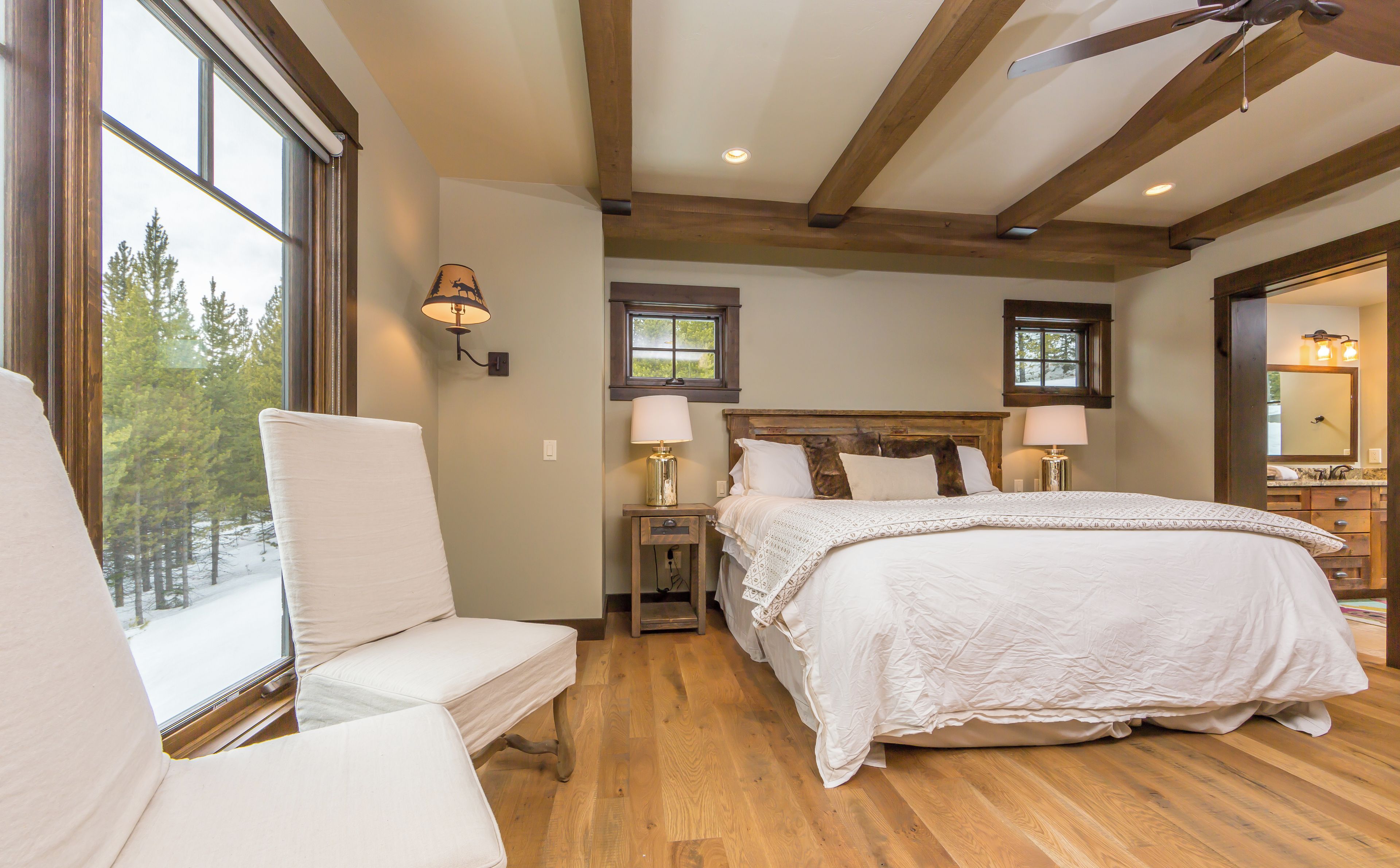 A bedroom with a large bed, two bedside lamps, a nightstand, and a window with a view of trees.