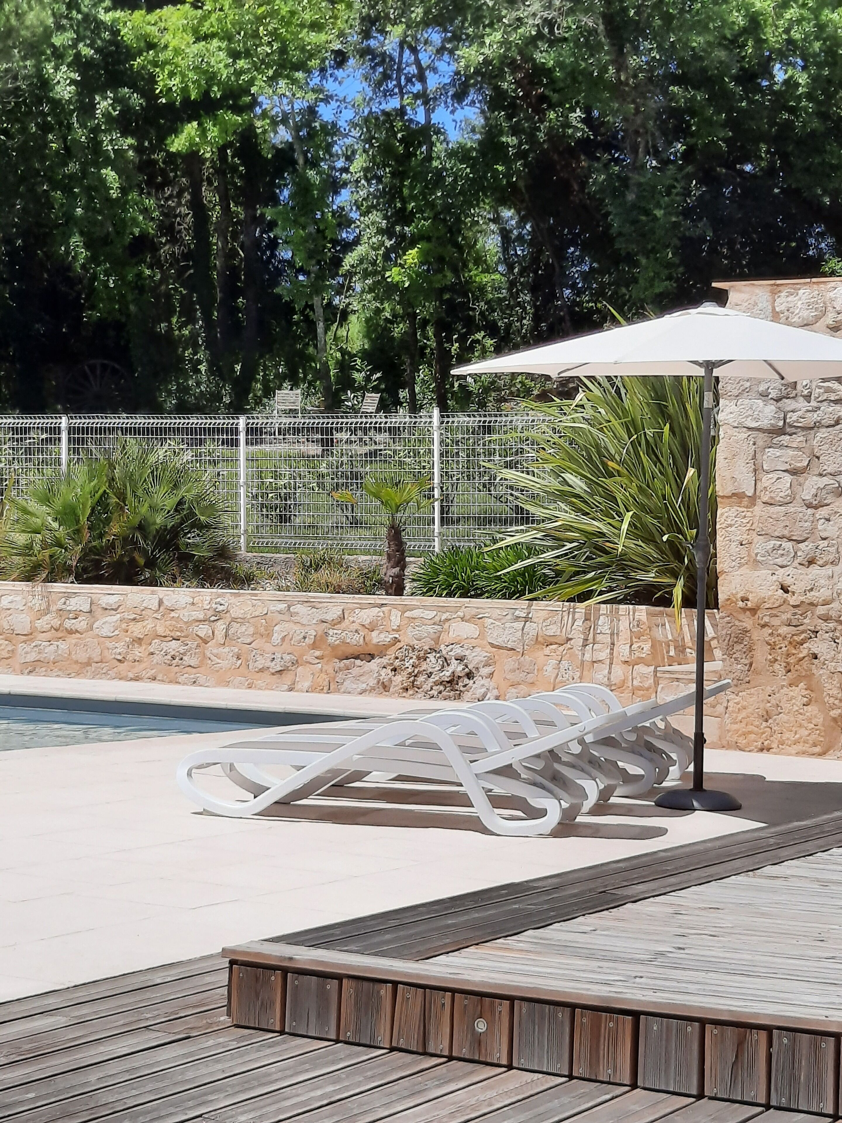 Un'area a bordo piscina con un muro in pietra, una recinzione metallica e un pontile in legno.
