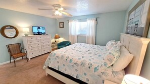 A bedroom with a bed, dresser, chair, television, and ceiling fan.
