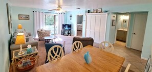 A living room with a television, sofa, and dining area with chairs and a table. - Sunsets #1502 Chateau La Mer II 2Bd-2Bath Ground Floor (Destin)