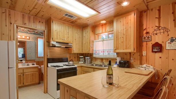 A wooden cabin kitchen with a central island, stove, sink, and various appliances. - (43R) Edna's Hearts Desire at The Redwoods In Yosemite (Wawona)