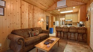A cozy cabin interior with a wooden interior, a sofa, a coffee table, and a kitchen area with bar stools. - (43R) Edna's Hearts Desire at The Redwoods In Yosemite (Wawona)